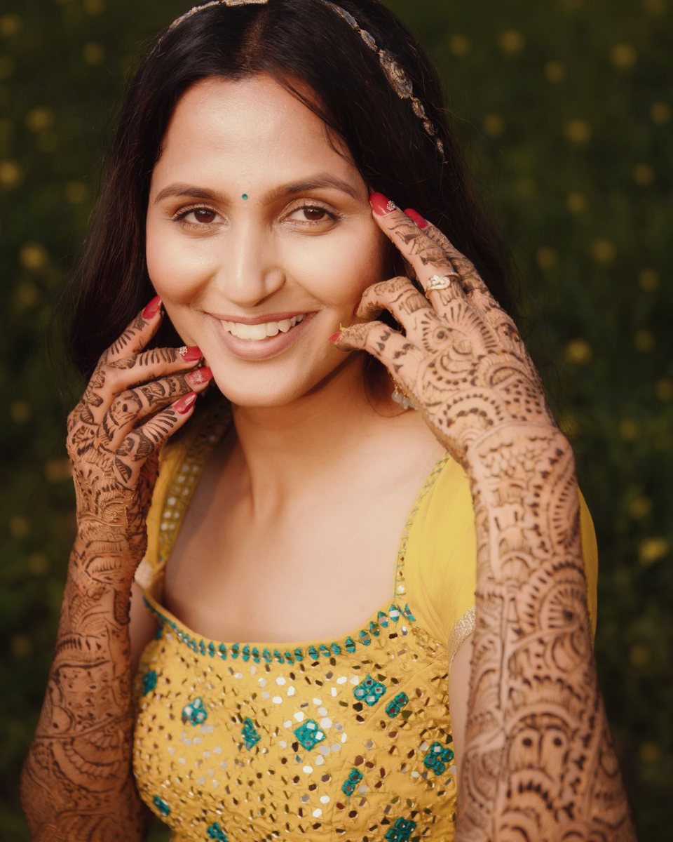 Aisha Rizvi, bridal makeup artist, smiling in traditional dress with henna on her hands